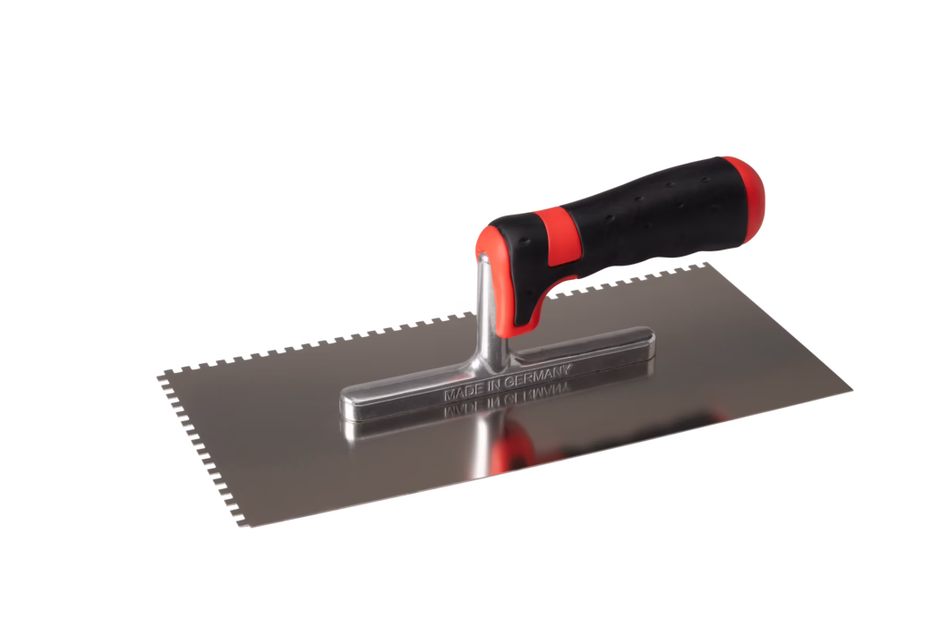 Pajarito_Dummy_Spreading trowel soft handle notched_017077_ 017082_017083_017085_017073_017087_017086_2021-02 Een getande roestvrijstalen troffel met een ergonomisch zwart-rood handvat, het blad gegraveerd met 'MADE IN GERMANY', gefotografeerd op een witte achtergrond.