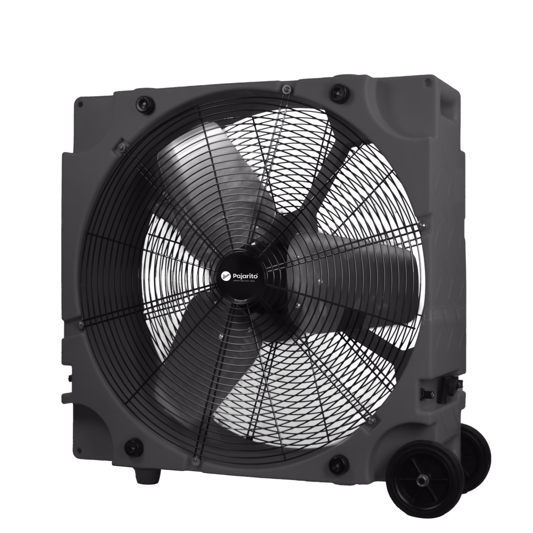 Pajarito_Dummy_Ventilator_181154_2024-08 Close-up of a large portable industrial axial fan housed in a rectangular plastic casing. The photo shows the front half of the fan with a black metal safety grille, three wide curved blades and a central hub labeled "Pajarito". The molded plastic frame features integrated handles, visible mounting points, rubber feet and two transport wheels at the bottom right. Screws and rubber vibration mounts secure the grille to the housing. High-contrast monochrome image highlighting the textures and details of the metal blades, grille and plastic housing.