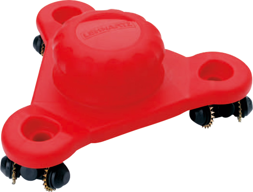 Pajarito_Dummy_Wallpaper tiger Easy Line_038498_2021-02 Close-up product shot of a bright red plastic furniture mover skate. The triangular, three-lobed plate features a raised central dome with a molded logo and three recessed circular pockets near each corner. Under the edges are black multi-wheel roller assemblies with small brass-coloured toothed sprockets visible. The image is cropped on a white background and highlights the textured plastic surface, the central dome detail and the roller mechanism used to slide heavy items across floors.