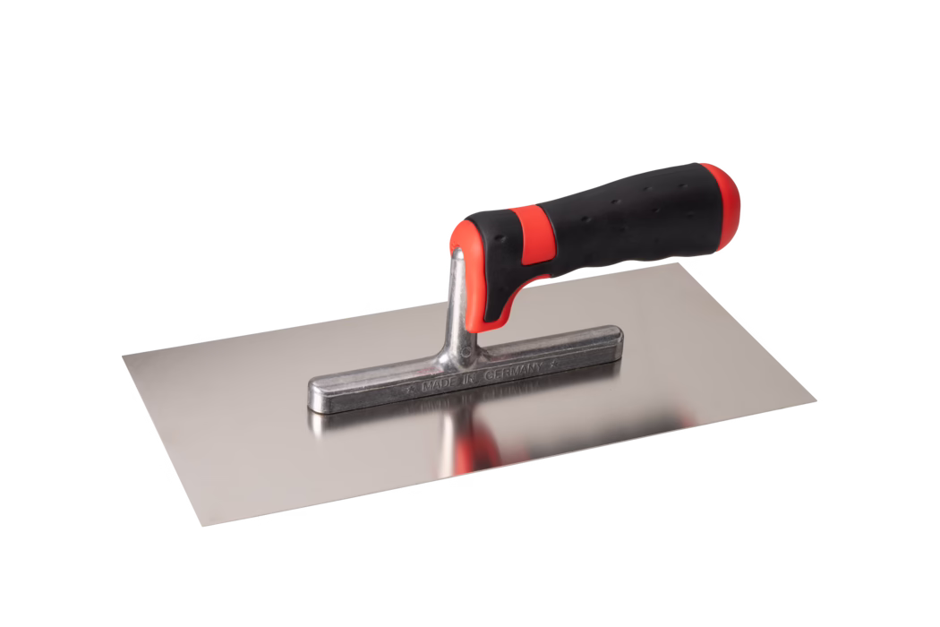 Pajarito_Dummy_Trowel soft handle Performance Line_034664_2021-02 Rechthoekige roestvrijstalen pleisterspaan met een glad vlak blad en een korte metalen hals die een ergonomische zwart-rode softgrip-handgreep draagt. Het gepolijste blad weerspiegelt lichtelijk de handgreep; de metalen hals is gemarkeerd met MADE IN GERMANY. De handgreep heeft rode accenten voor- en achteraan en een gestructureerd rubberen oppervlak voor extra grip. Het gereedschap is vrijstaand gefotografeerd op een witte achtergrond vanuit een iets verhoogde zijkantshoek. Geschikt voor het aanbrengen en gladstrijken van mortel, pleister of plamuur.