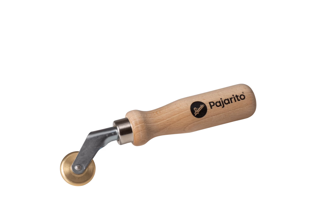 Handgereedschap met een glad, afgerond beukenhouten handvat bedrukt met de merknaam 'Pajarito', een korte metalen as en een klein messing rolwieltje op een draaibare beugel; bedoeld om naden, behangranden, leer of lijmoppervlakken aan te drukken en glad te strijken. De natuurlijke houtnerf en het zwarte logo zijn duidelijk zichtbaar. Foto op een witte achtergrond.
